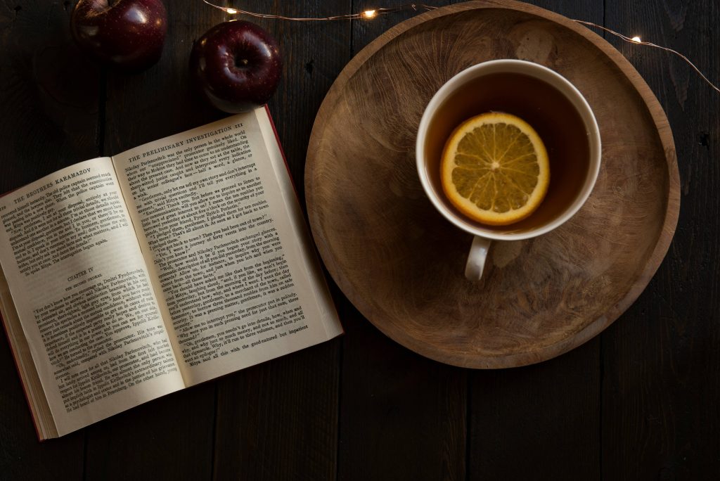 An open book and natural remedies for sore throat, a tea with lemon slice on top of a wooden plate